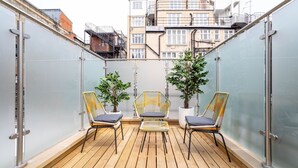 A balcony with wooden flooring, three wicker chairs with cushions, and two potted plants. - 3 Bedroom flat with Terrace in Central London (London)