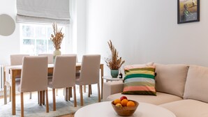 A modern living room with a beige sofa, a round coffee table with a fruit bowl, a dining area with a table and chairs, and a framed artwork on the wall. - 3 Bedroom flat with Terrace in Central London (London)