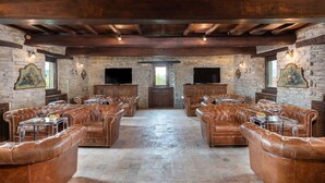 A spacious room with leather sofas, stone walls, and a wooden ceiling. - Villa Torre delle Rose by Geco Vacation Rentals (Visignano)