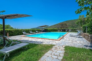 Piscina retangular com borda de pedra, rodeada por espreguiçadeiras e um pergolado.