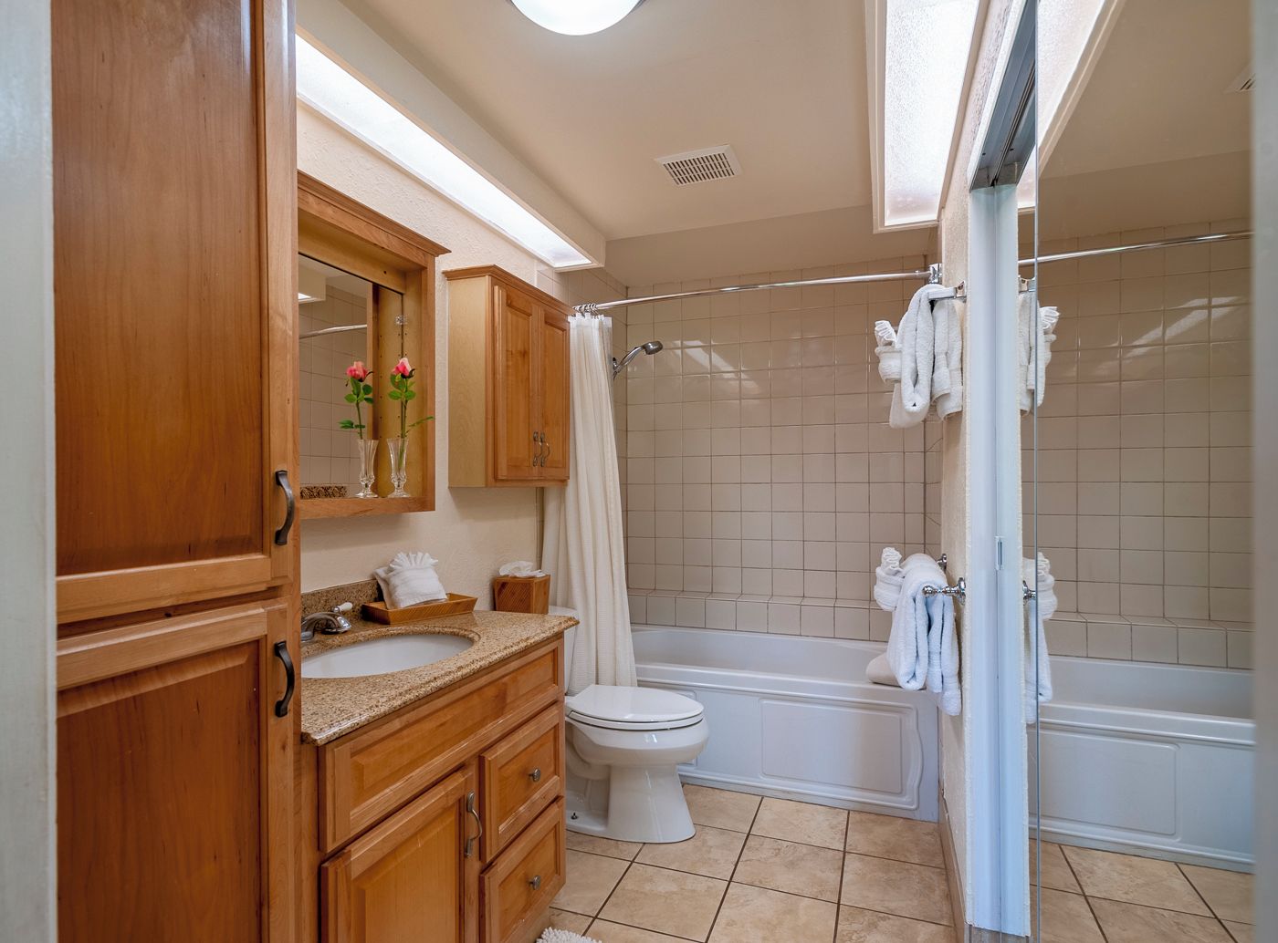 A bathroom with wooden cabinets, a sink, a toilet, and a bathtub with a shower curtain.