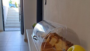 A buffet area with a covered display case containing bread and a bowl of fruit. - RAFKON Luxury Apartments - Myrina (Lemnos)