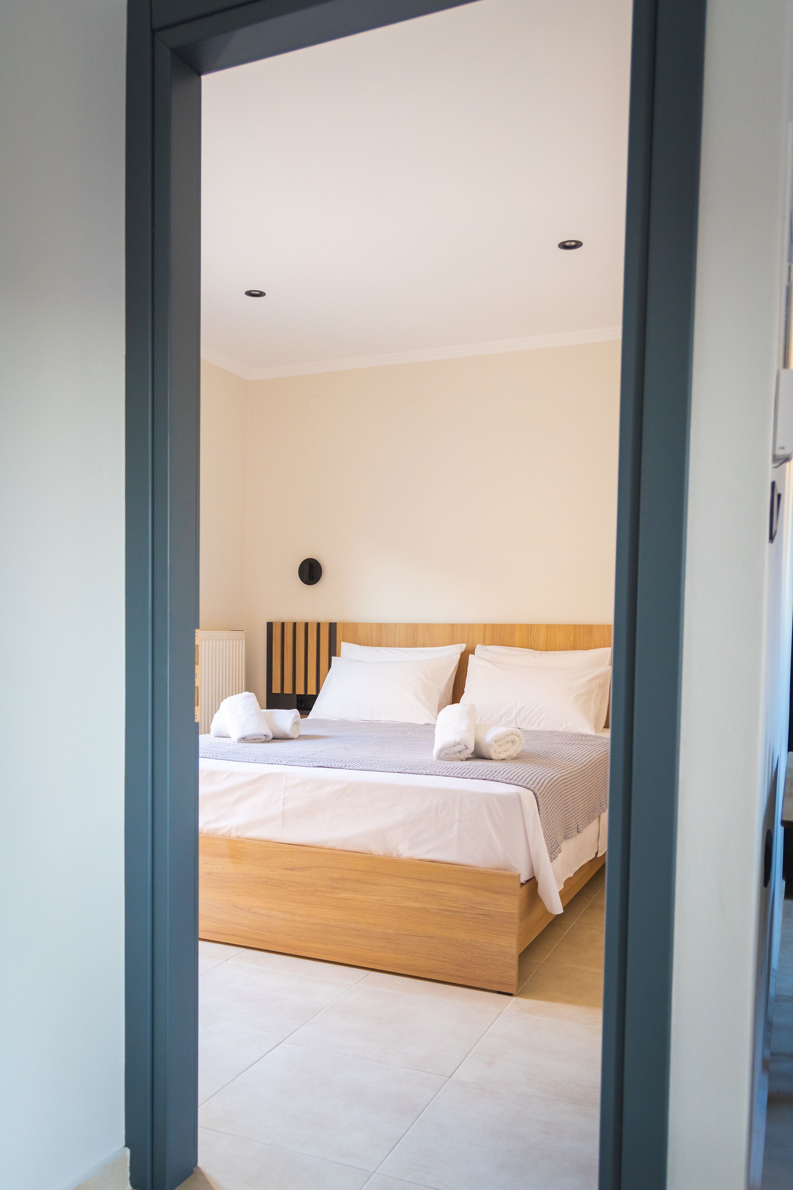 A modern bedroom with a wooden headboard, a large bed with white bedding, and a radiator on the wall.