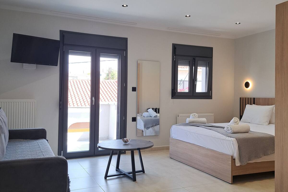 Una habitación de hotel moderna con cama, sofá, una mesita y televisor.