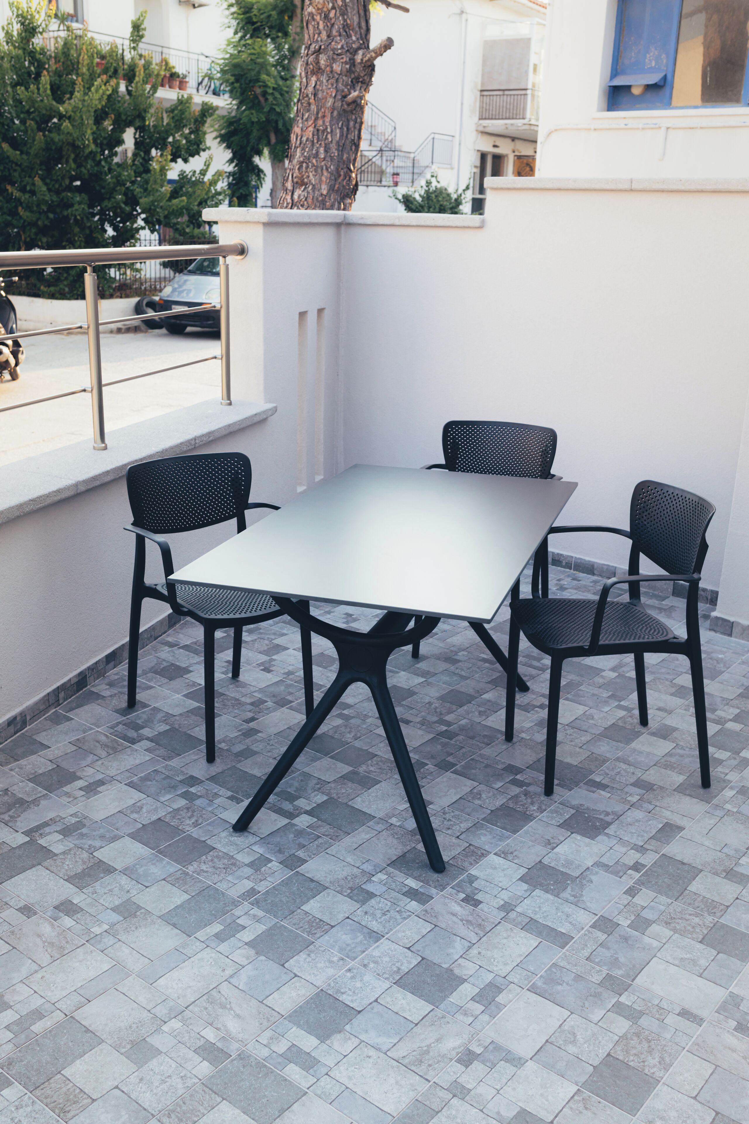 A patio with a table and four chairs, a railing, and a tree.