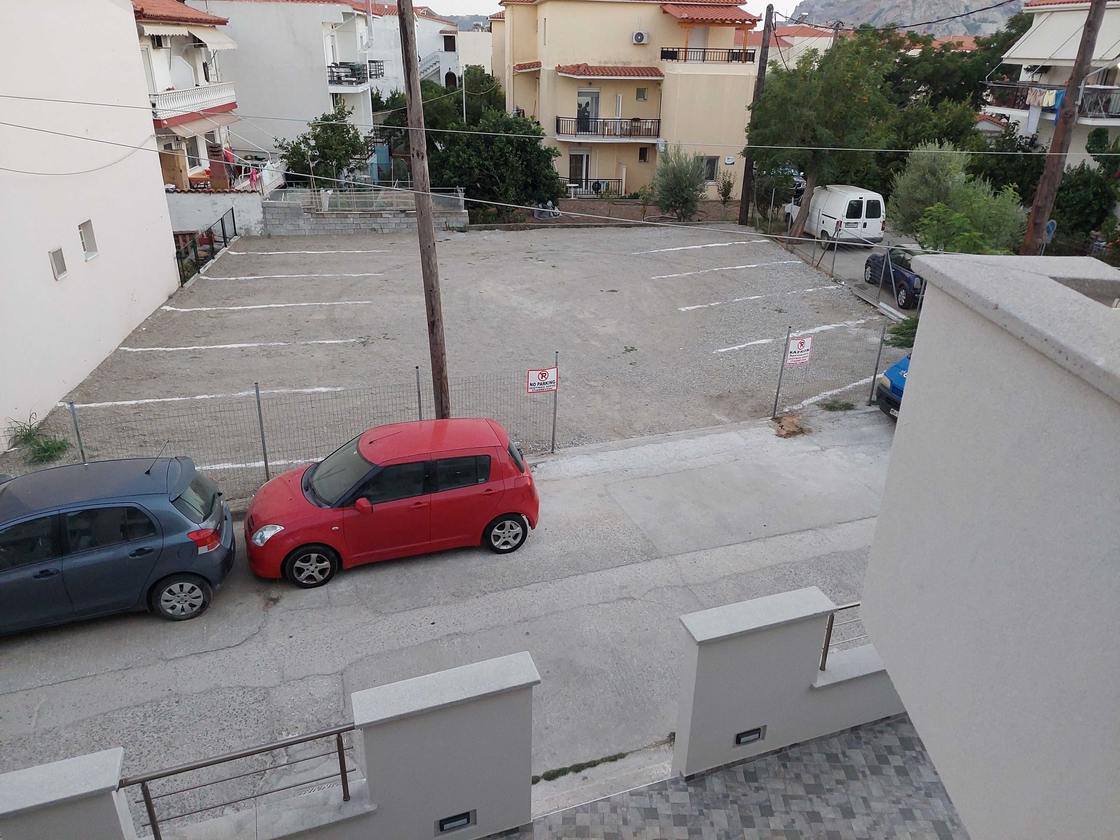 Ein Parkplatz mit zwei Autos, einem roten Kleinwagen, einer blauen Limousine und einem weißen Transporter im Hintergrund.