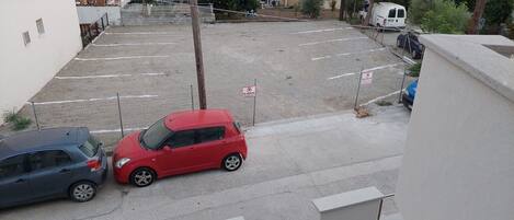 Ein Parkplatz mit zwei Autos, einem roten Kleinwagen, einer blauen Limousine und einem weißen Transporter im Hintergrund.