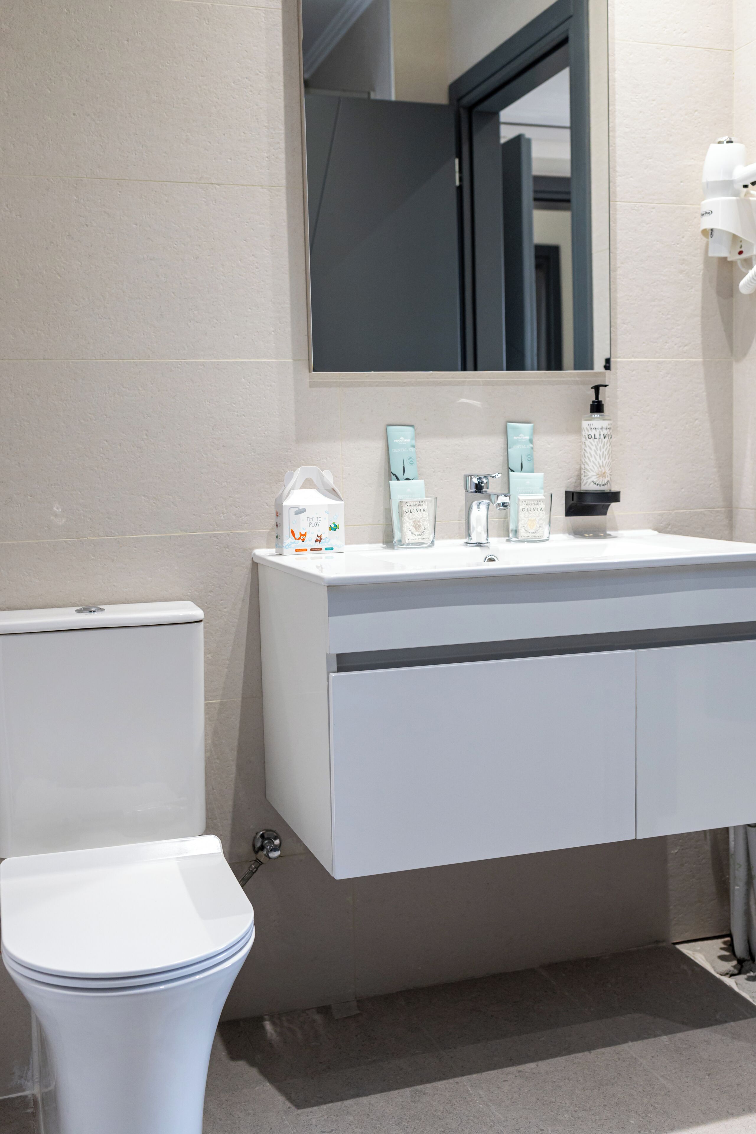 A modern bathroom with a white toilet, a sink with toiletries, and a mirror above the sink.