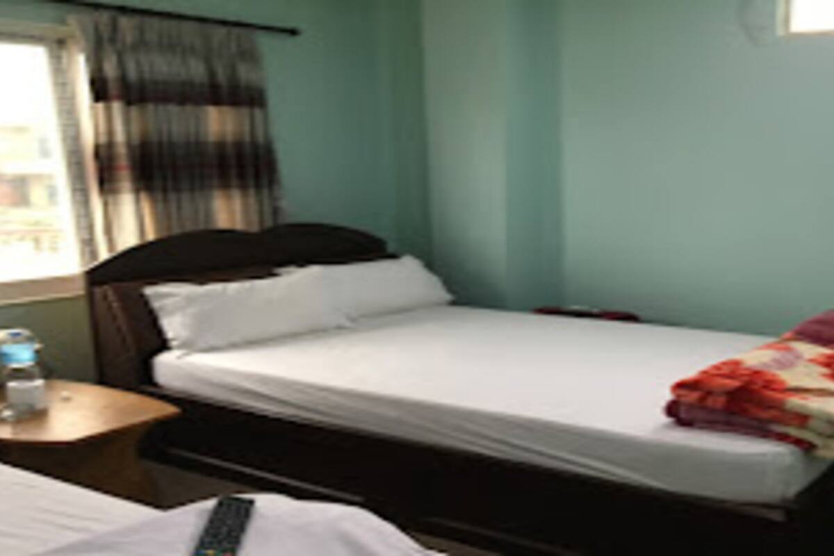 Een eenpersoonsbed in een kamer met een raam, een nachtkastje met een waterfles en een effen muur.