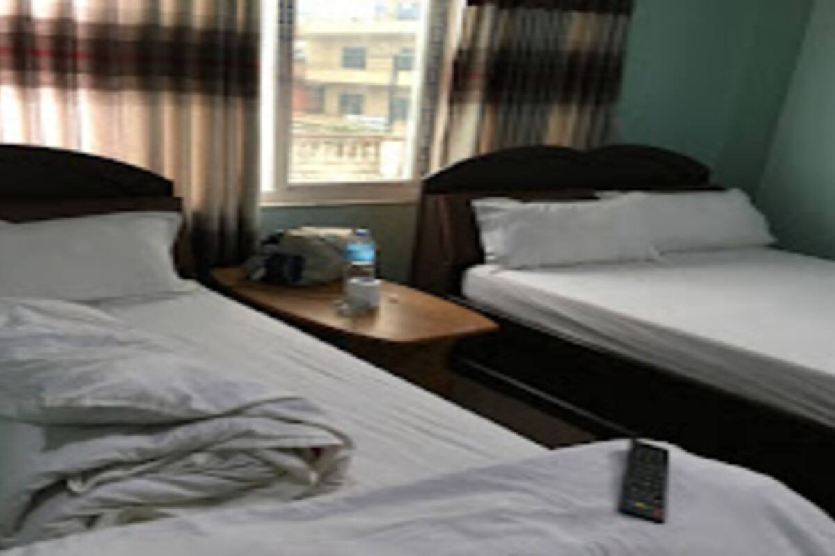 Een hotelkamer met twee eenpersoonsbedden, een nachtkastje met een fles water en een raam met gordijnen.
