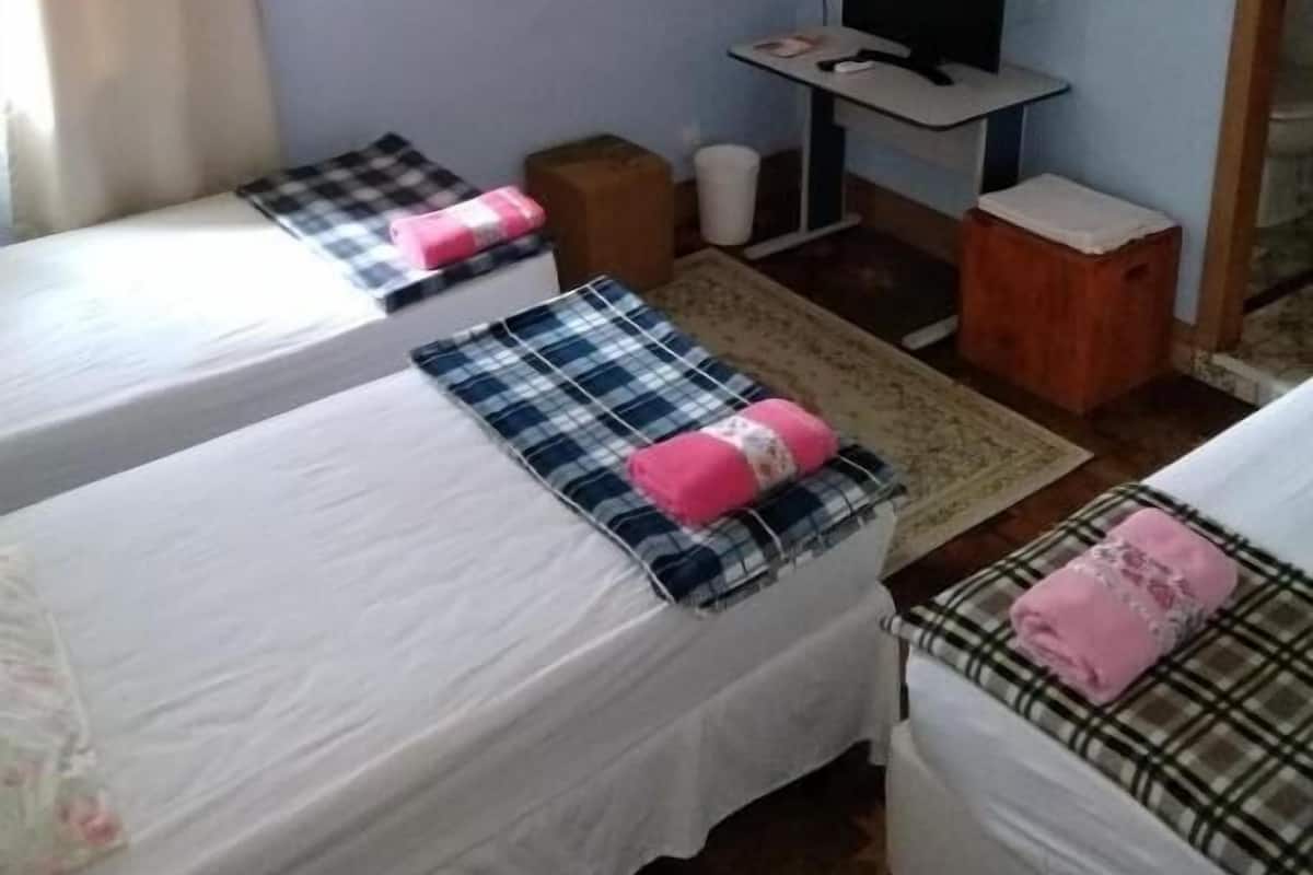 Quarto pequeno e simples com duas camas, uma escrivaninha, uma cadeira e uma televisão.