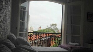 A room with a bed, a window, and a view of a balcony with a railing. - Ipê Rosa Hotel (Bauru)