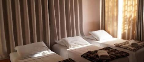 A hotel room with two beds, each with white linens and a plaid blanket on one bed.