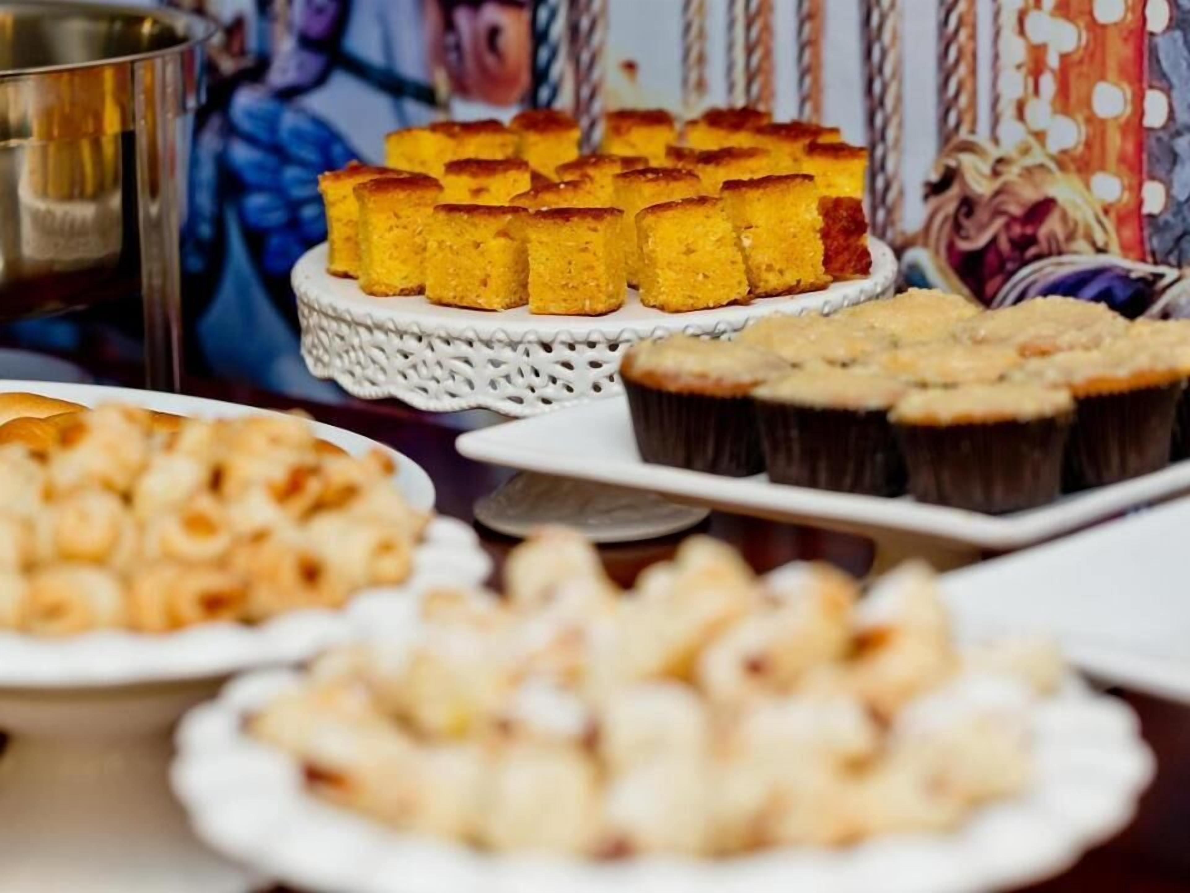 Esillä on monenlaisia leivonnaisia, kuten muffinseja ja kakku, joka on asetettu valkoiselle pitsialustalle.