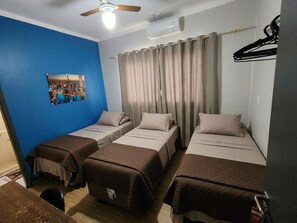 Una habitación con cuatro camas, ventilador de techo, equipo de aire acondicionado y un cuadro con una vista urbana.