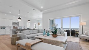 A spacious living area with a large sofa, a coffee table, and a view of the city through large windows. - Oceanfront 6 Bedroom Heated Pool Home in Cinnamon Beach! Barefoot Sands!! (Palm Coast)