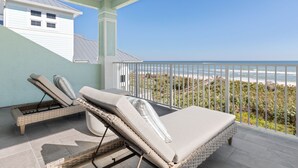 A balcony with two wicker lounge chairs, a view of the ocean, and a white building in the background. - Oceanfront 6 Bedroom Heated Pool Home in Cinnamon Beach! Barefoot Sands!! (Palm Coast)