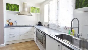 Eine moderne Küche mit weißen Schränken, Edelstahlgeräten und einem großen Fenster mit transparenten Vorhängen.