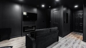 Une pièce moderne aux couleurs sombres, dotée d’un téléviseur à écran plat fixé au mur, d’un canapé noir et d’un plancher en bois.
