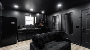 Une cuisine moderne avec des meubles de couleur sombre, un réfrigérateur noir et un canapé noir dans une pièce aux murs noirs et au plancher en bois.