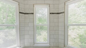 Habitación de esquina con tres ventanas amplias, paredes de azulejos blancos y un banco en la base.
