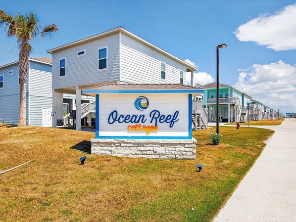 A sign for Ocean Reef cottages with a clear sky and a pathway leading to the buildings. - Turtle Cove 3 Bedroom Home by RedAwning (Rockport)
