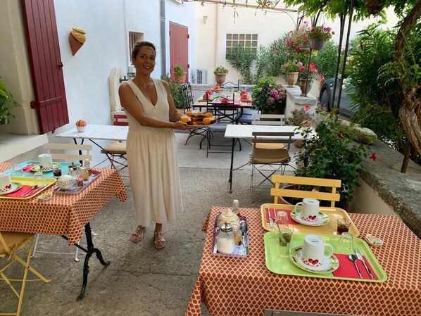 An outdoor dining area with tables set for a meal, surrounded by potted plants and a garden.