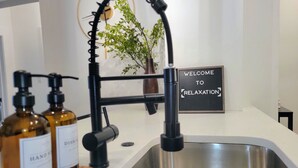 Une cuisine moderne avec un évier en acier inoxydable, un robinet noir et deux flacons de savon liquide. Une pancarte sur le mur indique : « BIENVENUE DANS UN HAVRE DE DÉTENTE ».