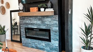Un salon moderne avec une cheminée en pierre, un téléviseur à écran plat fixé au-dessus, et une table basse en bois agrémentée d’objets décoratifs.