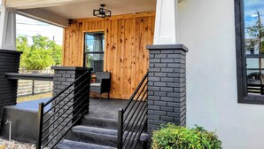 Une maison moderne avec une façade en bois, un porche abrité et un escalier menant à l’entrée.