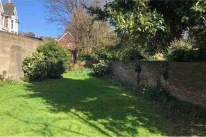 Stroll through the beautifully maintained garden, surrounded by lush shrubs and trees, with a traditional building in the background.