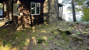 A rustic cabin with a stone chimney, wooden walls, and large windows.