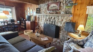A cozy cabin interior with a stone fireplace, wooden ceiling, and a comfortable seating area.