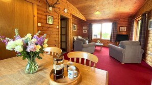 Een houten chalet van binnen, met een eethoek, een zithoek en een televisie.