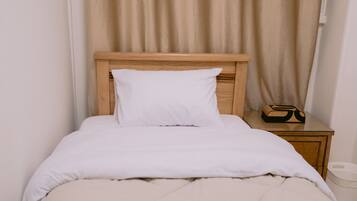 A neatly made bed with a wooden headboard, a white pillow, and a beige blanket.