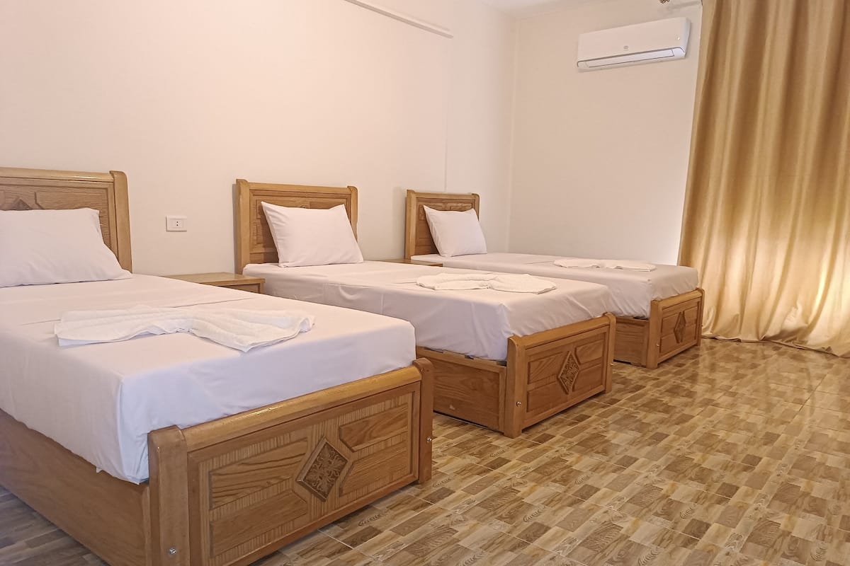 Hotellihuone, jossa on kolme puista sänkyä, valkoiset vuodevaatteet ja ruutukuviollinen lattia.