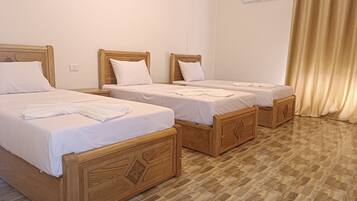 Habitación de hotel con tres camas de madera, ropa de cama blanca y suelo a cuadros.