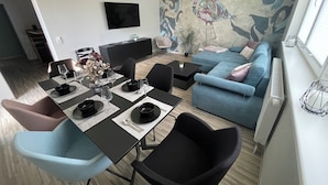 A modern living room with a dining area, a blue sofa, and a mural on the wall. - Modern vacation apartment "Stilapartment Oasis 1" close to the center (Wernigerode)