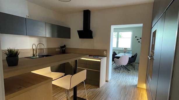 A modern kitchen with a central island, a dining area with a table and chairs, and a view into a dining room. - Modern vacation apartment "Stilapartment Oasis 1" close to the center (Wernigerode)