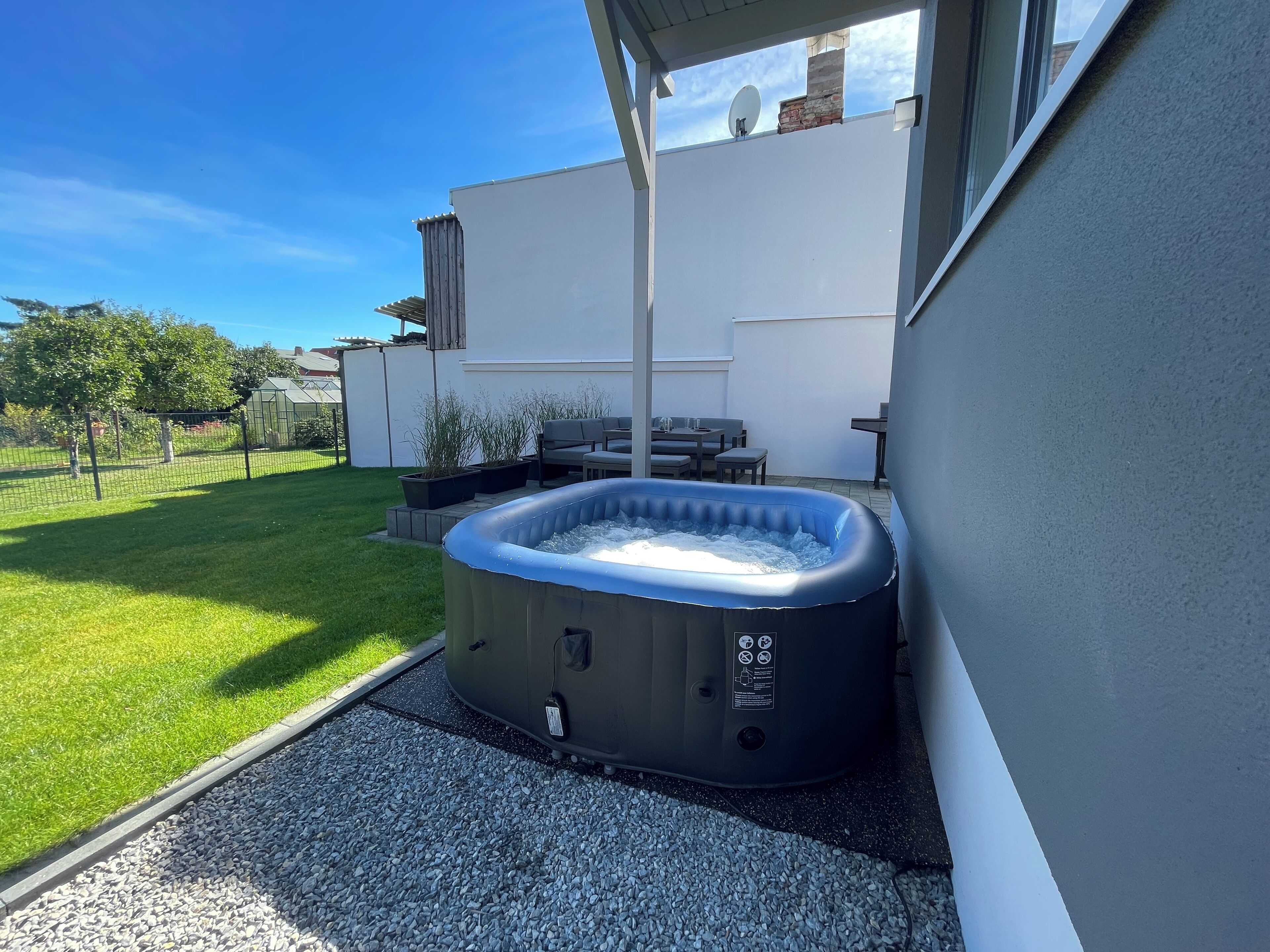 Ein Whirlpool in einem Garten mit Terrasse, einer weißen Wand und blauem Himmel.