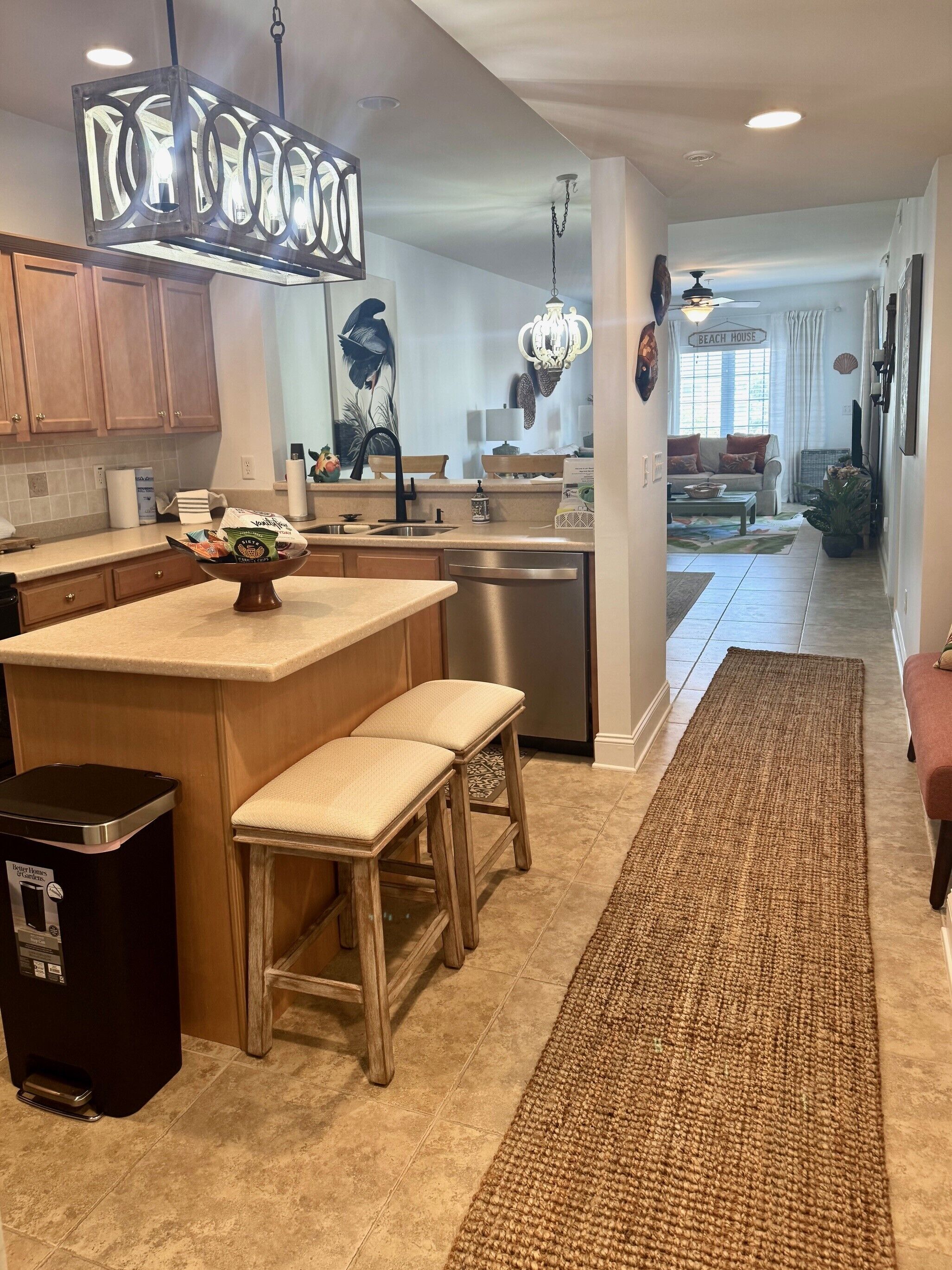 A modern kitchen with a central island, wooden stools, and a stainless steel dishwasher.