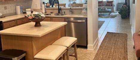 A modern kitchen with a central island, wooden stools, and a stainless steel dishwasher.