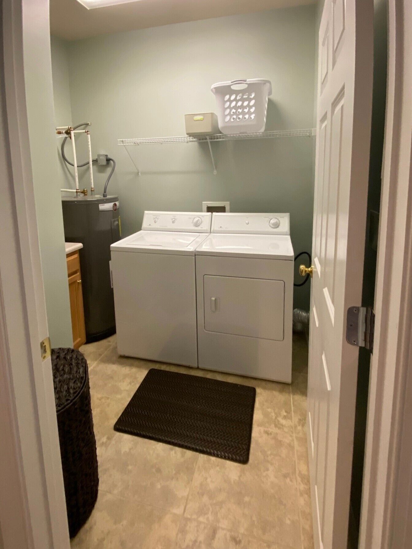 A laundry room with a front-loading washer and dryer, a utility sink, and a laundry basket on a shelf.