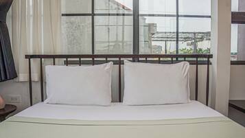 A hotel room with a large window, a bed with white bedding, and a view of buildings outside.