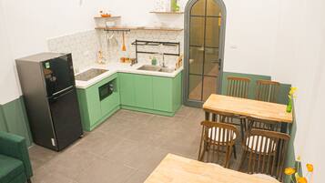 A compact kitchen with green cabinets, a black refrigerator, a wooden dining table with chairs, and a small sink.