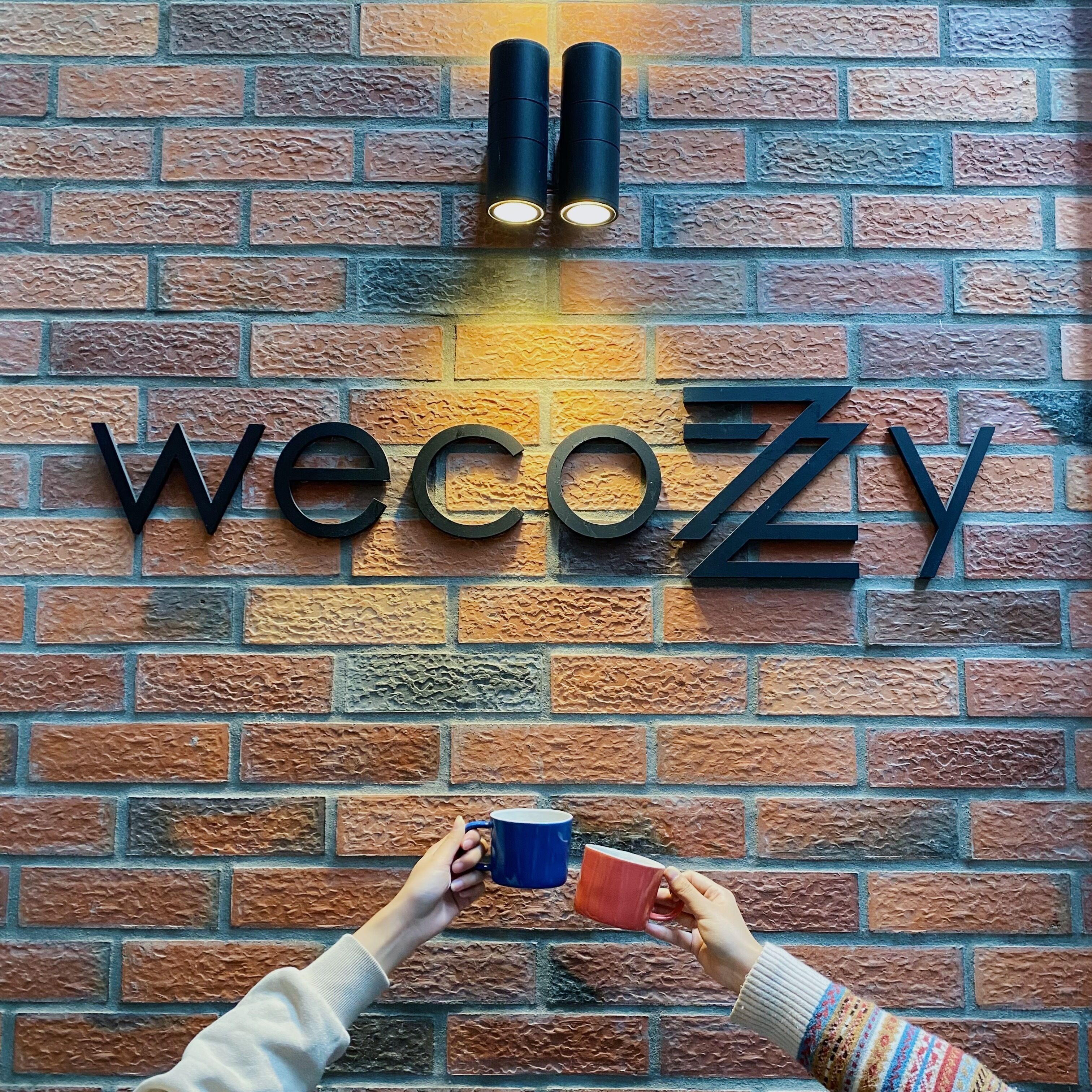A brick wall with the letters "wecozy" and two cylindrical lights.