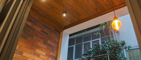 Una habitación con techo de madera, pared de ladrillo y ventana con vista a un edificio.