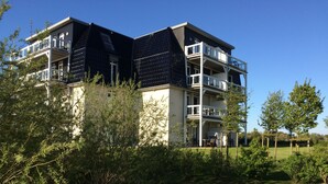 A multi-story residential building with balconies, surrounded by greenery and a well-maintained lawn. - Apartment "Moin im Deichgraf" on the Wremer beach and cutter harbor (Wurster Nordseeküste)