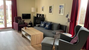 A living room with a sofa, armchairs, a coffee table, a TV, and artwork on the wall. - Apartment "Moin im Deichgraf" on the Wremer beach and cutter harbor (Wurster Nordseeküste)