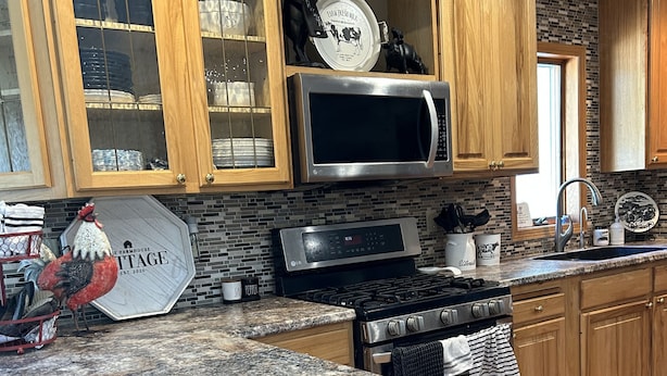 A kitchen with wooden cabinets, a stainless steel microwave, a gas stove, and a granite countertop. - Cozy and quaint farmhouse on an acreage  (Mountain Lake)